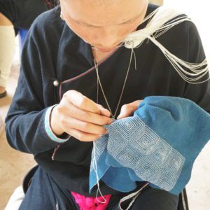 Lanten artisan stitching a geometric design on clutch