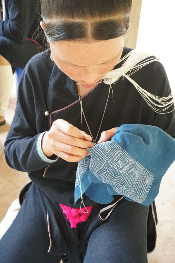 Lanten artisan stitching a geometric design on clutch